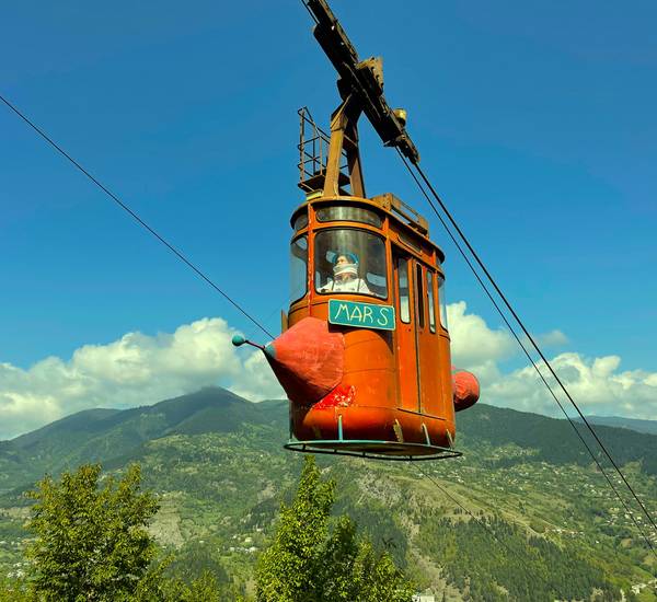 schwebende rostrote Gondel einer Seilbahn mit grünen Berg im Hintergrund